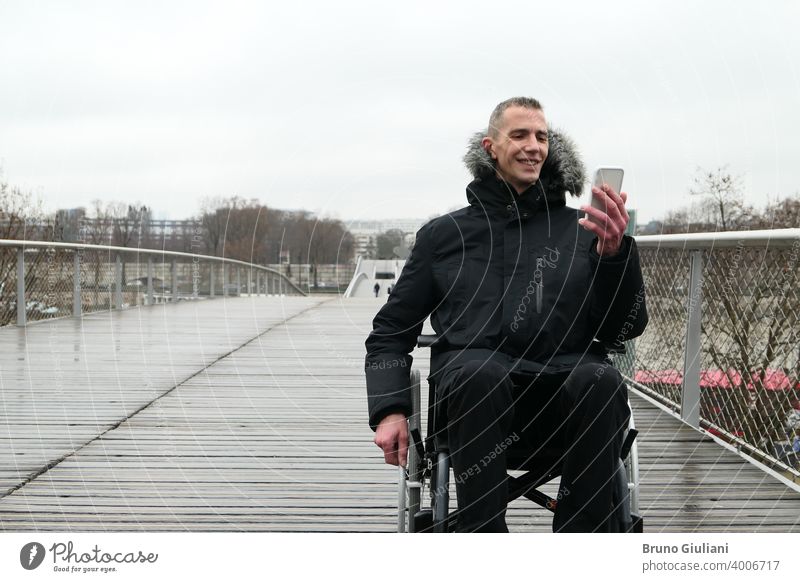 Konzept der behinderten Person. Mann in einem Rollstuhl draußen auf der Straße. Menschen mit Technologie mit Smartphone. Gerät querschnittsgelähmt verbunden