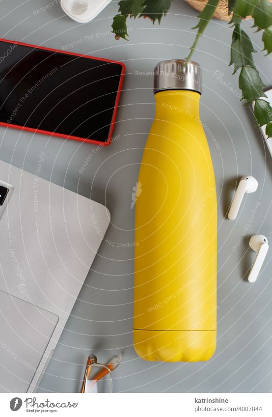 Gelbe Isolierflasche auf grauem Schreibtisch umgeben von modernen Gadgets und Pflanze gelb Flasche eingeschnitten wiederverwendbar Attrappe Vase Draufsicht