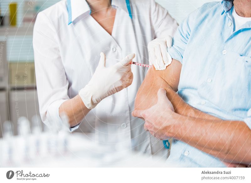 Eine Ärztin mit chirurgischer Maske und in Handschuhen gibt einem Mann im Krankenhaus eine Impfstoffinjektion. Impfung während der COVID-19-Pandemie Arme Pflege