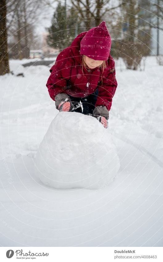Ein Mädchen rollt eine große Schneekugel für den Bau eines Schneemanns Farbfoto Gedeckte Farben Tag Außenaufnahme Schwache Tiefenschärfe Natur natürlich