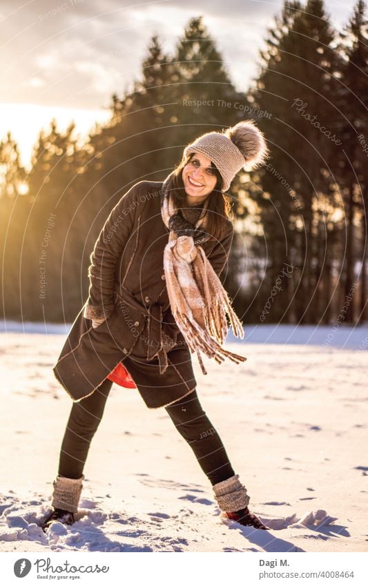 Lebenslustige Frau steht auf einem schneebedeckten Feld am Waldrand im Hintergrund Wintersonne Lebensfreude Winterwonderland Schnee Mütze Schal Freude