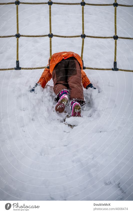 Ein Kind liegt im Schnee und spielt im Spielplatz-Netz Tag Außenaufnahme natürlich Tiefenunschärfe Leben Freude kalt kalte jahreszeit weggucken Winter Kälte 1