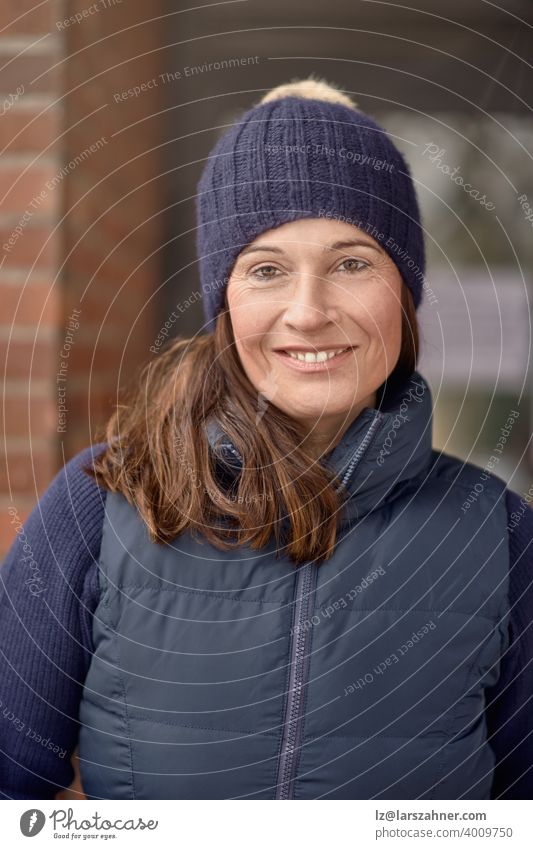 Attraktive freundliche lächelnde Frau in blauem Winteroutfit mit gestrickter Mütze und warmer Jacke in einer Nahaufnahme Kopf und Schultern Outdoor-Porträt