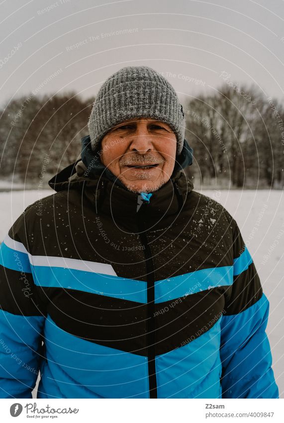 Portrait eines sportlichen Rentners rentner mann alter daunenjacke winter kälte mütze lachen freundlich natürlich portrait draußen warme farben aufrichtig