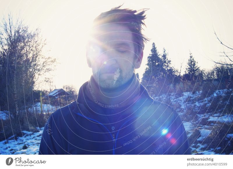 Mann beim Sonnetanken (in Winterlandschaft im Gegenlicht) Strahlen Gesicht Haare kalt frostig wärmend geschlossene Augen Blendflecken blau entspannt genießen