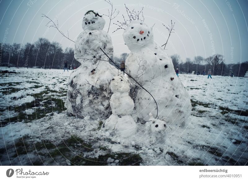 Fröhliche Schneefamilie, gebaut aus Schnee und Dreck auf großer Wiese, sich neigend, da es schon zu warm ist Eis Schneemann Schneefrau Schneekind Familie