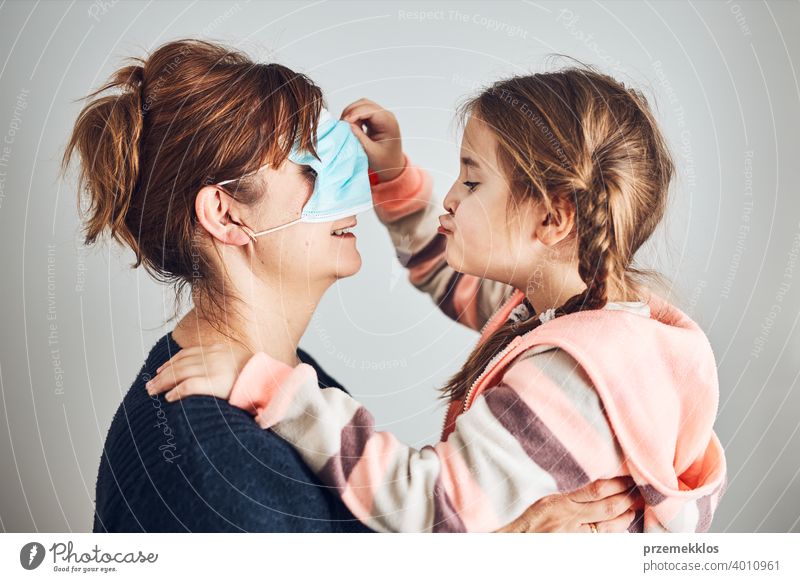 Kleines Mädchen bewegt die Gesichtsmaske ihrer Mutter auf die Augen und gibt ihrer Mutter einen Kuss. Lustige Momente während der Covid-19-Pandemie Zuneigung