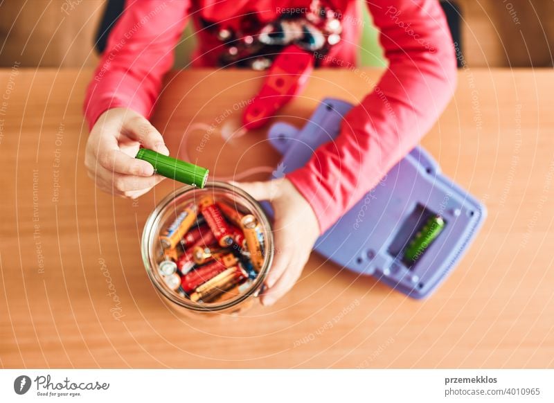 Kleines Mädchen, das verbrauchte Batterien aus einem Spielzeug entfernt und in ein Gefäß zum Recycling legt Behälter Kind sammelnd Konzept konzeptionell