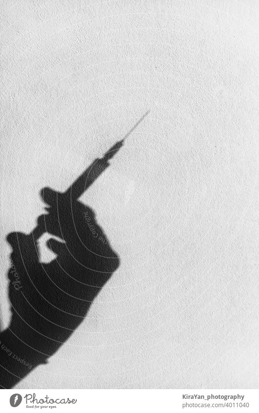 Schatten einer Hand mit einer Spritze auf einer weißen Wand covid-19 Coronavirus Gesundheit Impfung Konzept medizinisch schwarz auf weiß Textfreiraum