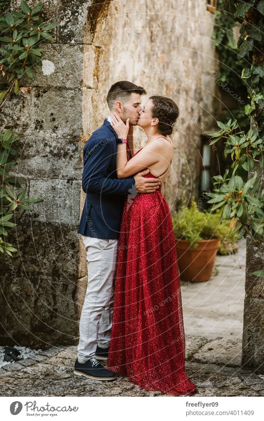 Elegantes junges Paar auf einem luxuriösen Gebäude mit Vegetation elegant Abschlussball Kuss 20s Kleid Anzug rot erstes Mal Veranstaltung Kaukasier Reichtum