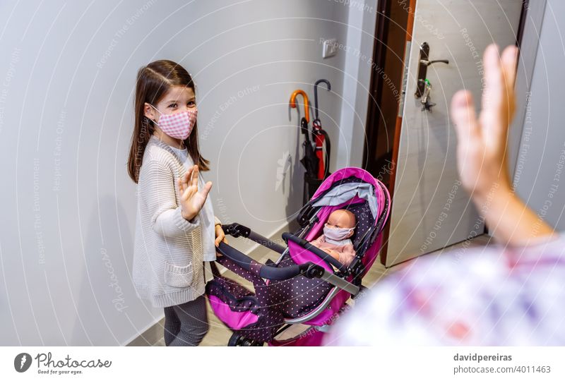 Mädchen mit Maske bereit, für einen Spaziergang mit ihrer Puppe mit Maske sagen auf Wiedersehen zu seiner Mutter zu gehen Coronavirus Schutzmaske