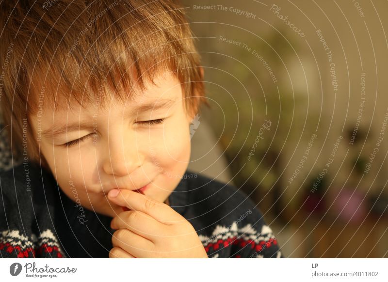 Kind mit geschlossenen Augen lächelt in die Kamera und versucht, etwas zu essen Zukunftsaussichten Kinderspiel geheimnisvoll friedlich Lächeln Anschluss Moment