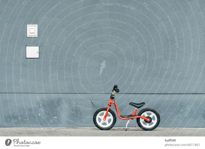 ein rotes Laufrad, geparkt vor grauer Wand  - Pause Kinderrad kinderlaufrad minimalistisch Fahrrad Fahrradfahren Kindheit Rad Lifestyle Bewegung Verkehrsmittel
