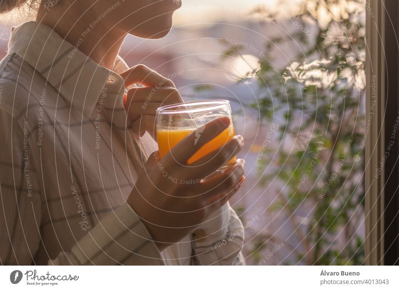 Junge Frau, die einen frisch gepressten Orangensaft zu Hause genießt. jung trinken Glas hübsch Kristalle Morgen früh neben Fenster Frische Licht halb-abgedeckt