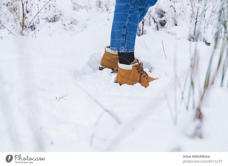 Füße in gelben, orangefarbenen Stiefeln, Beine in Blue Jeans im Schnee. Wanderung, Outdoor-Erholung. Mädchen, Frau geht in schönen Winterwald blau Jeanshose