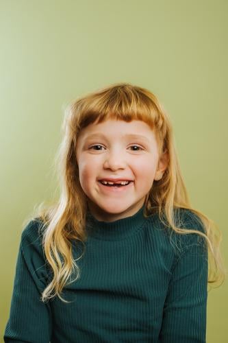 Porträt eines lachenden blonden Mädchens vor grünem Hintergrund Pony blondes Haar Freizeitkleidung Kind Kindheit farbiger Hintergrund niedlich Tochter Emotion