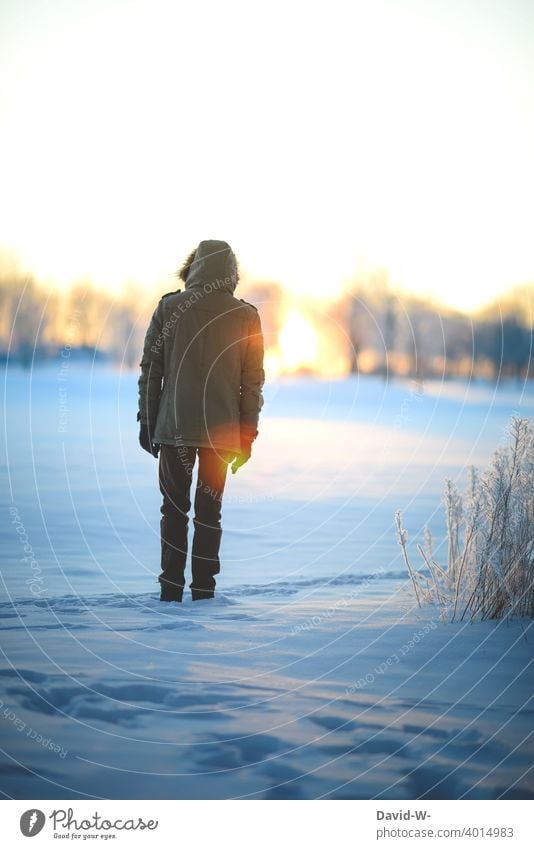 Winter - Mann steht im Sonnenlicht auf einer verschneiten Lichtung und genießt die letzten Sonnenstrahlen des Tages Wintertag Schnee Sonnenuntergang genießen