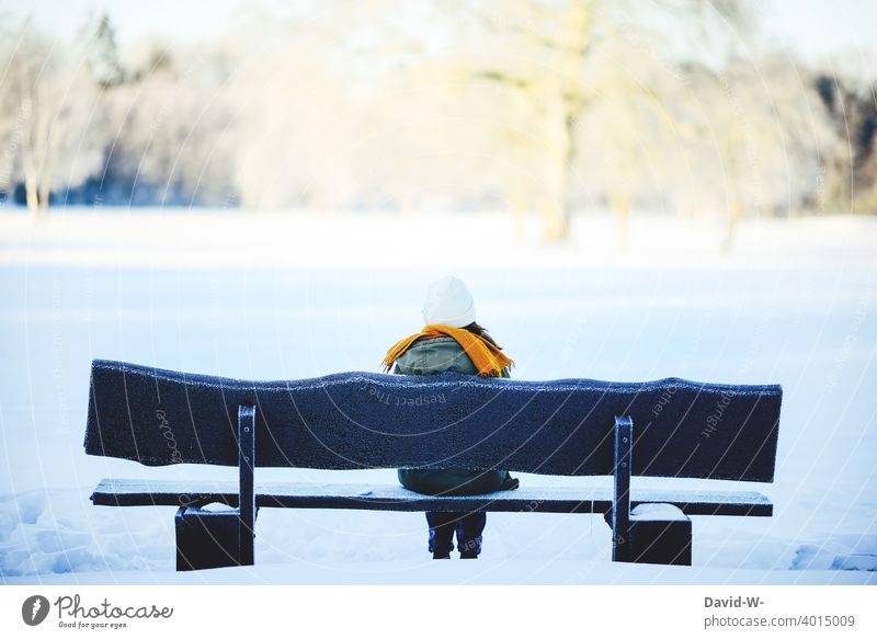 junge Frau sitzt an einem kalten Wintertag auf einer Bank in der Natur Landschaft sitzen Schnee genießen Ruhe Wintereinbruch Winterstimmung weiß