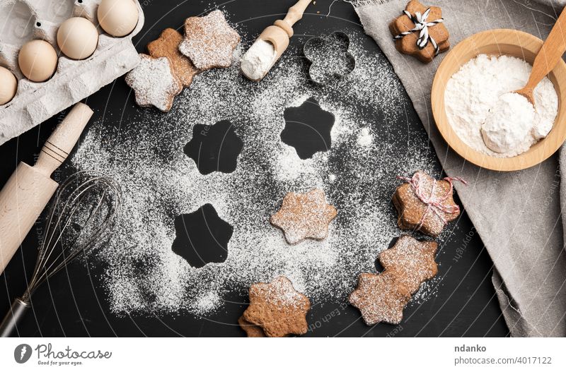 Sternförmig gebackene Lebkuchenplätzchen mit Puderzucker bestreut auf einem schwarzen Tisch Keks Mehl Bestandteil Serviette Ei Teller Löffel rollierend