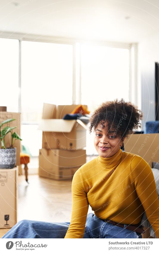 Porträt der jungen Frau, die auf dem Boden sitzt und lächelt, während sie in ein neues Haus umzieht, das von Kisten umgeben ist Hauskauf Auspacken heimwärts