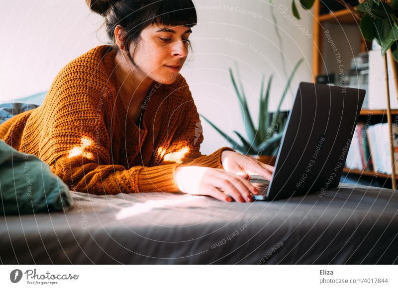 Eine Frau liegt zuhause auf dem Bett und arbeitet mit ihrem Laptop im Home Office Homeoffice Notebook arbeiten surfen online liegen gemütlich Lifestyle