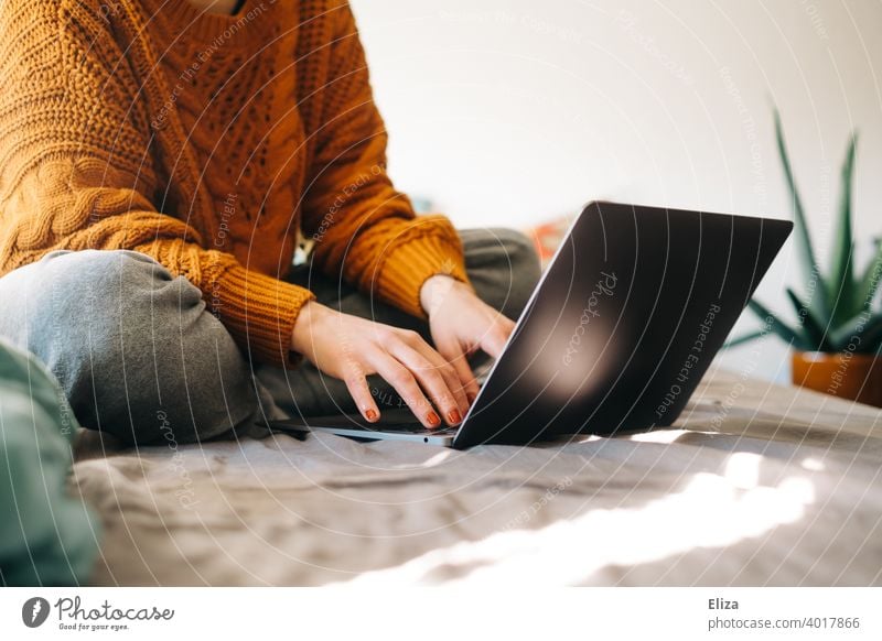 Junge Frau sitzt zuhause auf dem Bett und tippt etwas auf dem Notebook Laptop online surfen arbeiten Homeoffice home office tippen Computer modern Lifestyle