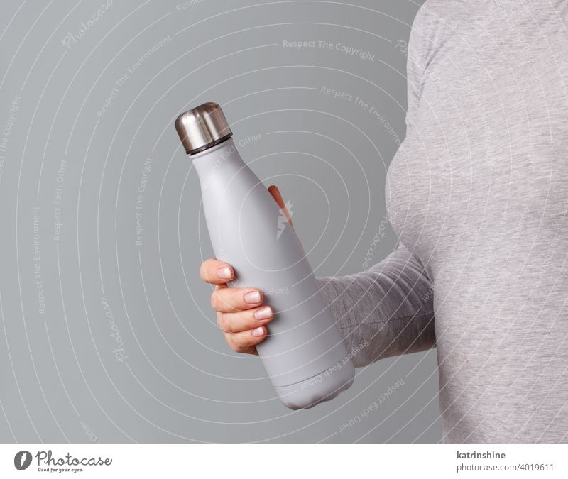 Frau in grauem T-Shirt hält graue isolierte Flasche auf grauem Hintergrund wiederverwendbar Hand Körper Monochrom ökologisch Wasser Stahl Thermo offen Halt hell