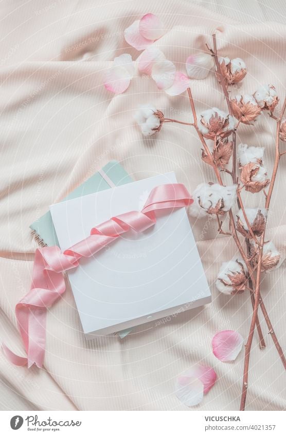 Ästhetischer Lebensstil. Notizbuch, weiße Box mit rosa Schleife. Beigefarbener Stoffhintergrund mit Baumwollzweigen.  Ansicht von oben. Ästhetik Lifestyle