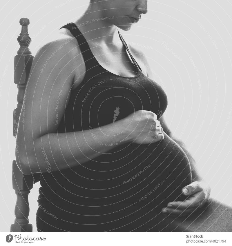 Hübsche junge schwangere Frau sitzt am Fenster im Zimmer Schwangerschaft Bauch heimwärts bw blaack Stuhl schön Glück Baby Leben Pflege Mutter Person