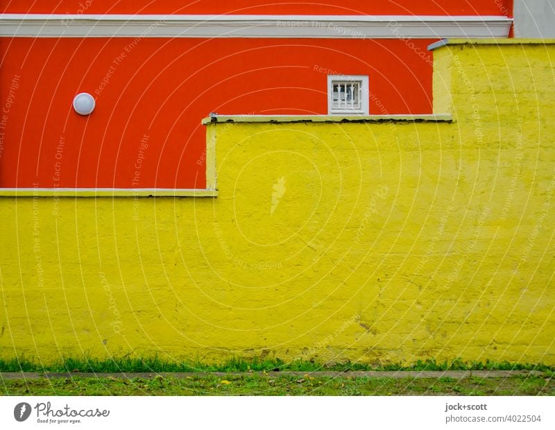 stufige Mauer trifft auf knallige Hauswand Fassade orange kleines Fenster Architektur Außenleuchte Stuck Putz gelb Wiese grün Anordnung Farbfläche Farbkontrast
