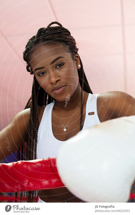 Porträt der schönen jungen afroamerikanischen Frau, die in die Kamera schaut und Boxhandschuhe im Boxring in einer Turnhalle trägt. Training Afro-Look Boxsport