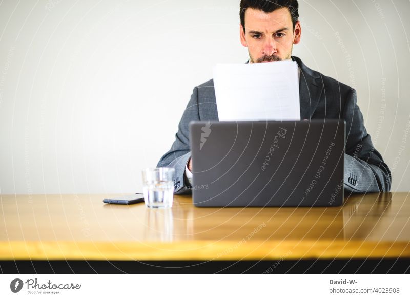 am Schreibtisch arbeiten - Mann am Laptop laptop Notebook Homeoffice Computer Arbeitsplatz konzentriert kontrollieren Dokumente überprüfen skeptisch Büro