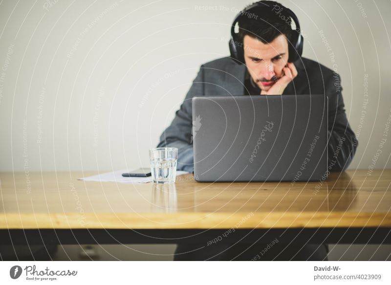 Mann arbeitet am Laptop / Notebook Tisch arbeiten sitzen konzentriert Headset surfen online business Arbeitsplatz zu Hause Homeoffice Prüfung