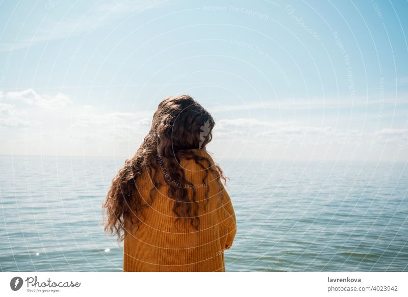 Rückenaufnahme einer Frau in einem gelben Pullover, die am Strand vor dem Wasser steht, MEER Meer reisen Urlaub Mädchen Feiertag jung Ausflug Rückseite Sommer