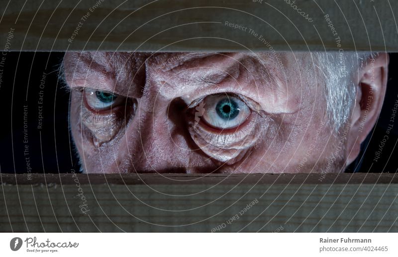 Ein älterer Mann blickt intensiv und unheimlich aus der Dunkelheit ins Licht Blick Blickkontakt böse bedrohlich Blick in die Kamera maskulin gruselig Wut