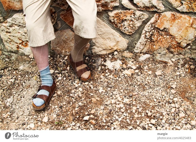 Ein Mann trägt Sandalen mit unterschiedlichen Socken Mode Beine Fuß Außenaufnahme Mauer steinig Schuhe Kuriosität steiniger weg Mensch Hose Erwachsene Tag