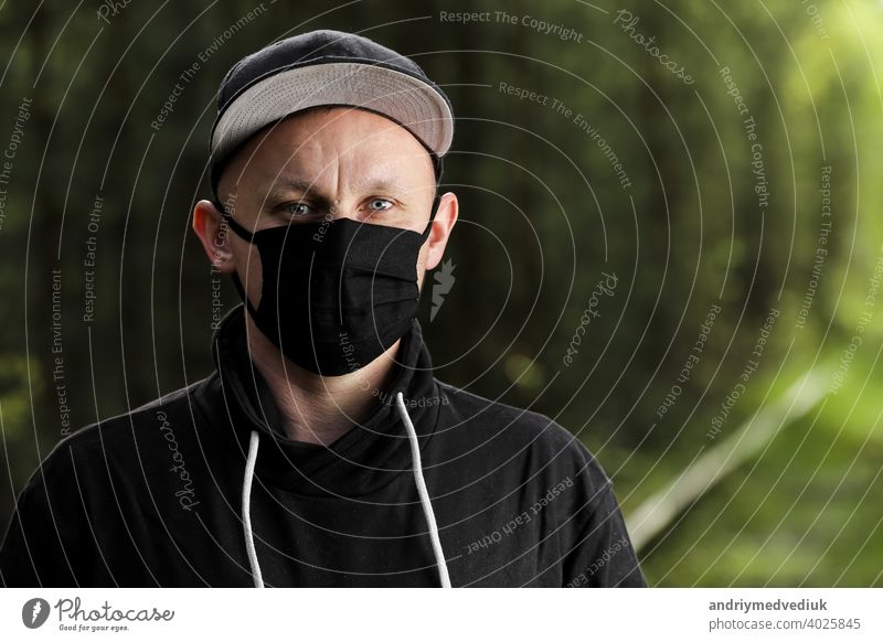 Junger Mann in schwarzer antiviraler Schutzmaske im Sommerpark. Der Kerl ruht im Freien an einem sonnigen Sommertag in einer Maske von seinen eigenen Händen gemacht. Virenschutz. Quarantäne-Maßnahmen