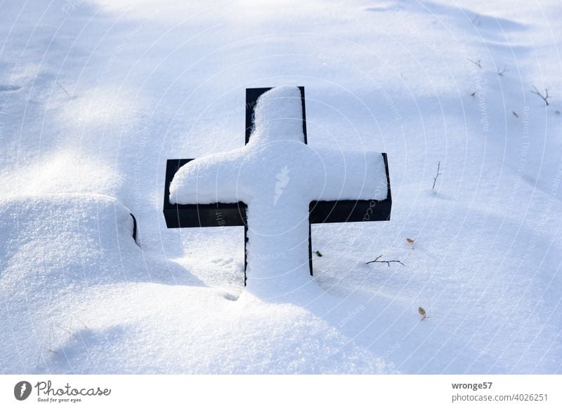 Ein mit Schnee bedeckter liegender Grabstein in Kreuzform auf einem verschneiten Grab Grabkreuz christliches Symbol Winter Schneedecke Grabstelle Grabstätte