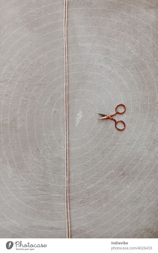 Eine kleine roségoldene Schere und ein Stück Seil auf grauem Hintergrund. Garn geschnitten Roségold Hobby diy Aktivität Pause Nahaufnahme Konzept Handwerk