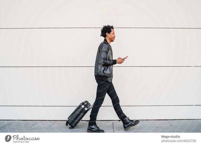 Tourist, der sein Mobiltelefon benutzt und einen Koffer im Freien trägt. Mann Mobile Telefon Mitteilung Business Text schwarz Zelle SMS benutzend Feiertag