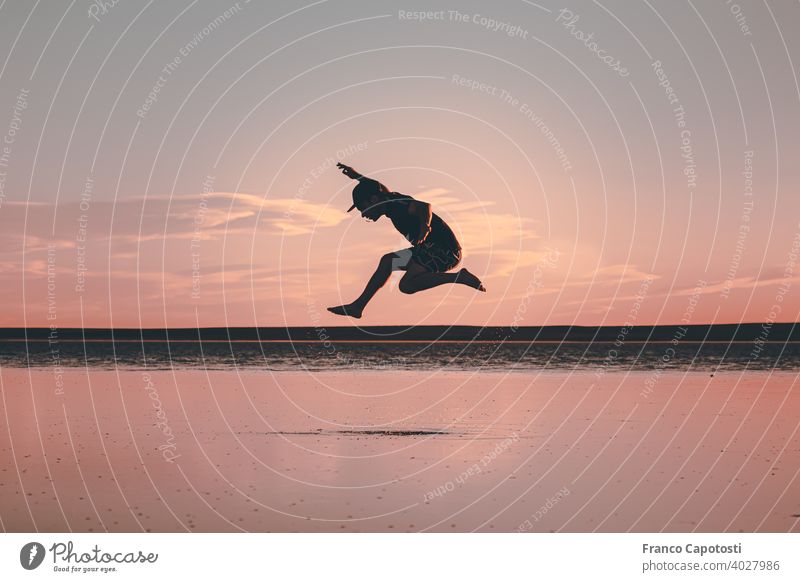 junger Mann springt am Strand springend fliegen Freiheit frei Sport Wolken Himmel Silhouette See Wasser Schönes Wetter Sommer Gegenlicht Fröhlichkeit
