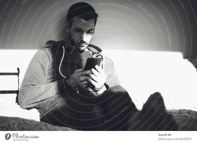 Mann benutzt sein Handy und liegt im Bett benutzen Sonnenlicht Schatten Licht lesen Nachricht Internet social media Student Chatten Frust ernst