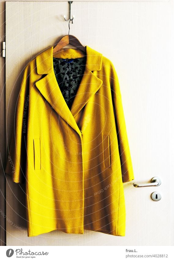 Ein Mantel hängt am Haken Innenaufnahme Übergangsmantel Tür Türklincke Kleiderbügel gelb Mode auffällig neongelb Sommermantel