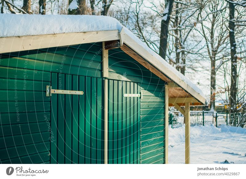 grüne Holzhütte im Winter bei Schnee im Wald Bauwerk Dach Haus Holzfassade Tor Tür Waldrand grünes Holz Außenaufnahme Farbfoto Menschenleer Hütte Gebäude