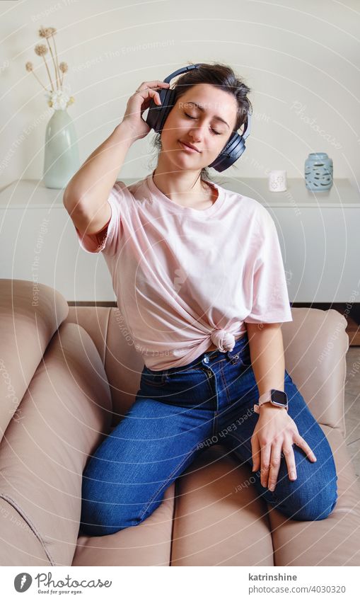 Junge Frauen, die mit Kopfhörern Musik hören jung anhaben Attrappe T-Shirt Lifestyle Jeanshose im Innenbereich Sofa Liege Rundhals lässig Brötchen Person