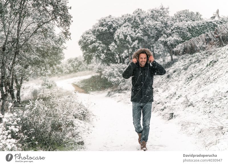 Lächelnder Mann in Oberbekleidung spazieren im Wald im Winter Spaziergang schlendern Schnee Schneefall genießen heiter Wälder kalt Saison warme Kleidung Jacke