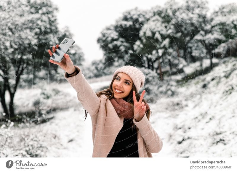lächelnde Frau nimmt Selfie im Winter fotografieren Wald Smartphone Schnee Gedächtnis Wälder Moment warme Kleidung schlendern Landschaft benutzend Gerät kalt