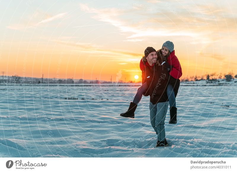 Glückliches Paar mit Spaß in verschneiten Feld Huckepack Winter Schnee Spaß haben heiter Landschaft Liebe Zusammensein Mitfahrgelegenheit Freude Lachen