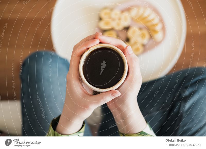 Frau hält eine Tasse mit schwarzem Kaffee, Aufnahme direkt von oben. Beim Frühstück, Morgenkaffee zu Hause trinken schwarzer Kaffee Körperteile Nahaufnahme