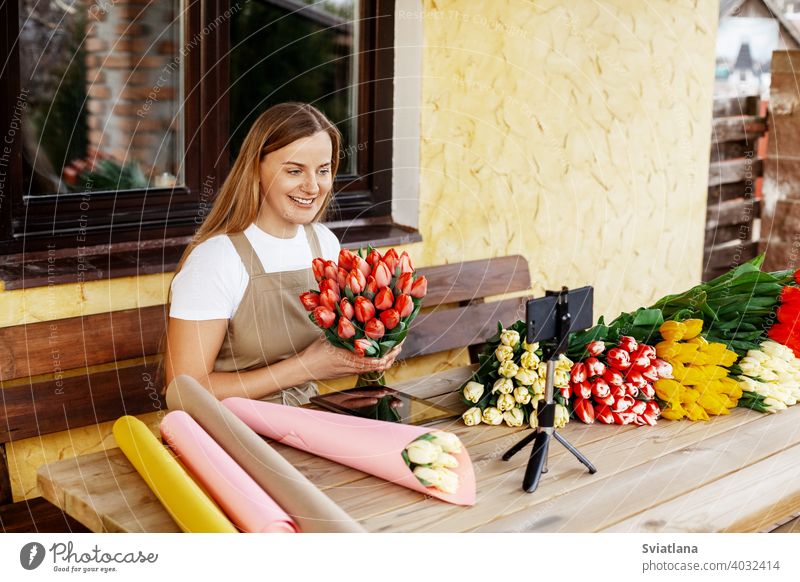Eine junge Floristin packt in ihrem Geschäft Tulpensträuße und dreht eine Video-Masterclass für ihren Blog. Frauentag und Valentinstag Telefon Blumenhändler